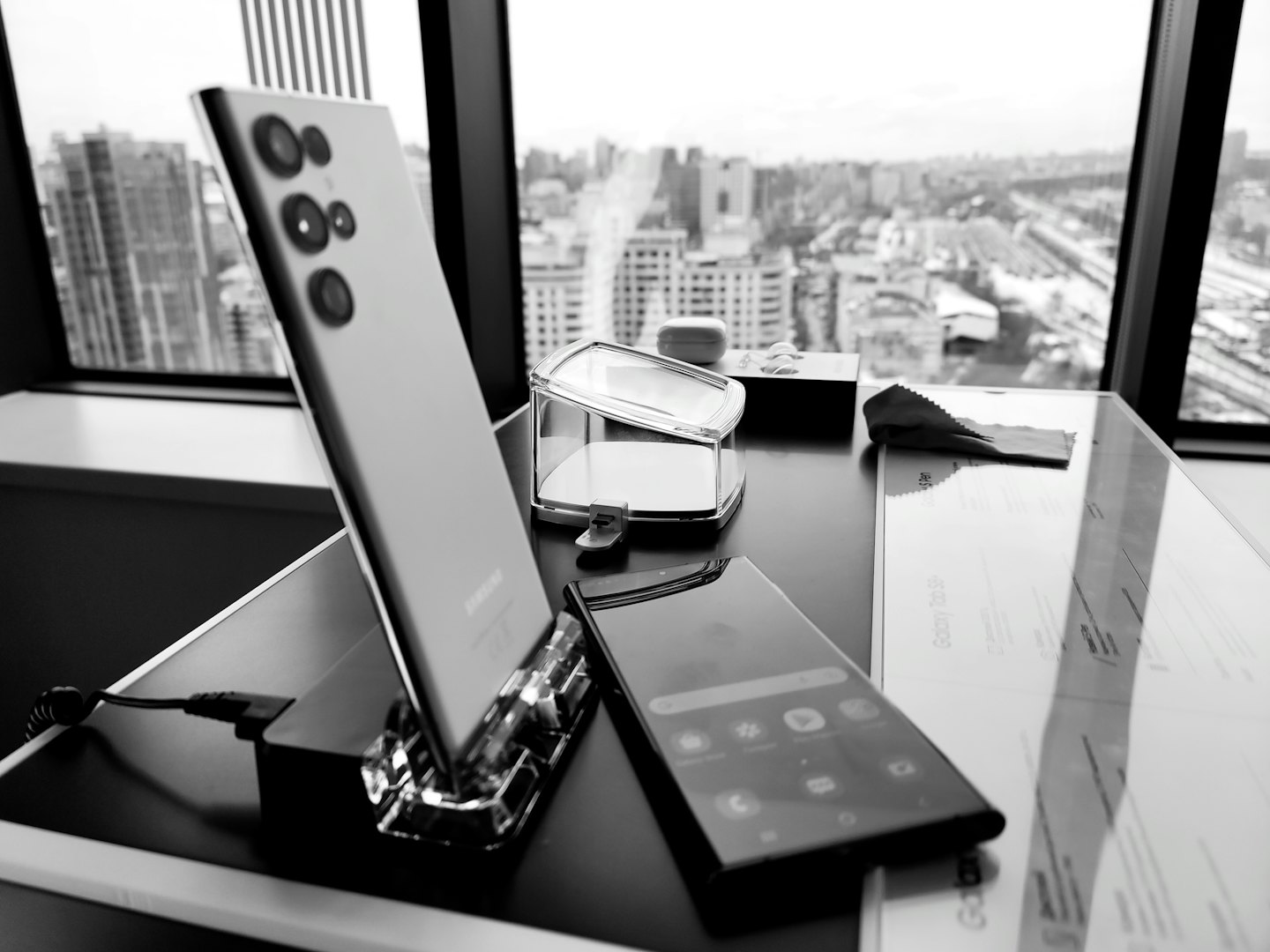 Two smartphones and accessories sit on a desk overlooking city tracks.